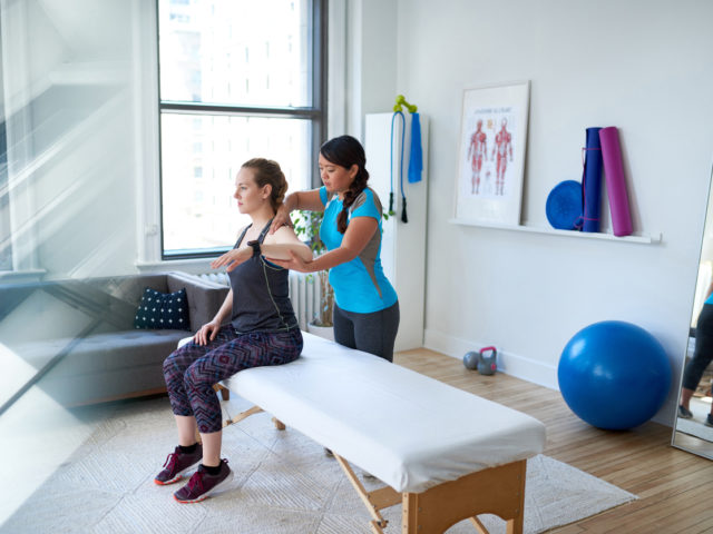 Chinese woman physiotherapy professional giving a treatment to an attractive blond client in a bright medical office
